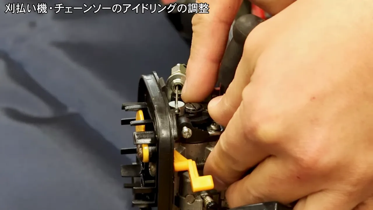 指でアイドリング調整ネジを確認しているキャブレターのクローズアップ写真。