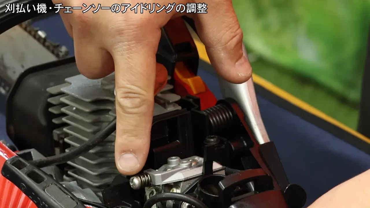 調整ネジを指で指し示すチェーンソーのキャブレターのクローズアップ