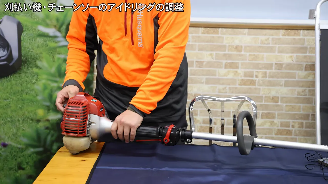 刈払い機のエンジンを両手で押さえ、キャブレター周辺を確認する様子