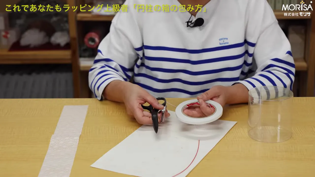 両面テープ、ハサミ、包み紙、透明な円柱容器がテーブル上に並んでいるクローズアップ