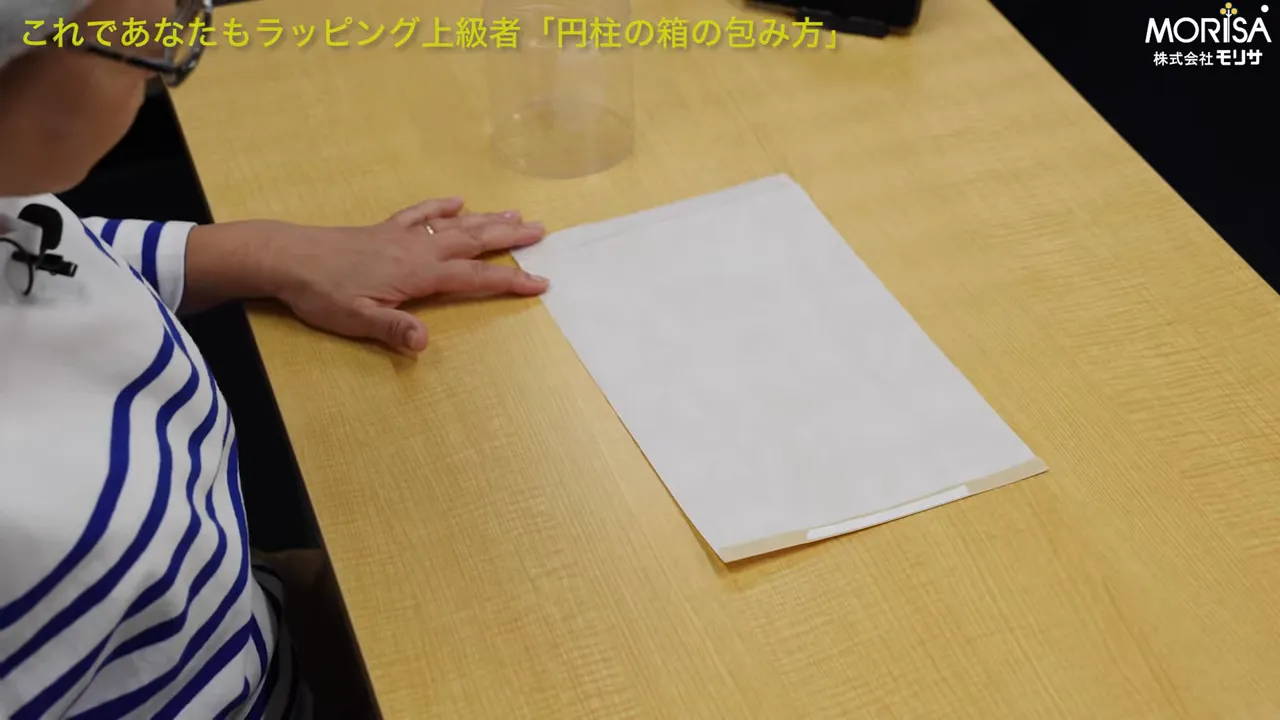 円柱包み用の紙に両面テープが貼られている様子、テーブルの上に広げた状態