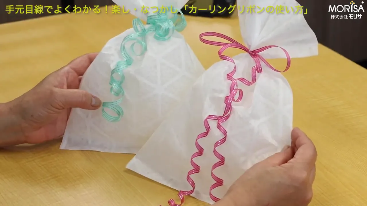 ピンクと緑の複数本のカーリングリボンをまとめた完成した包みの手元。