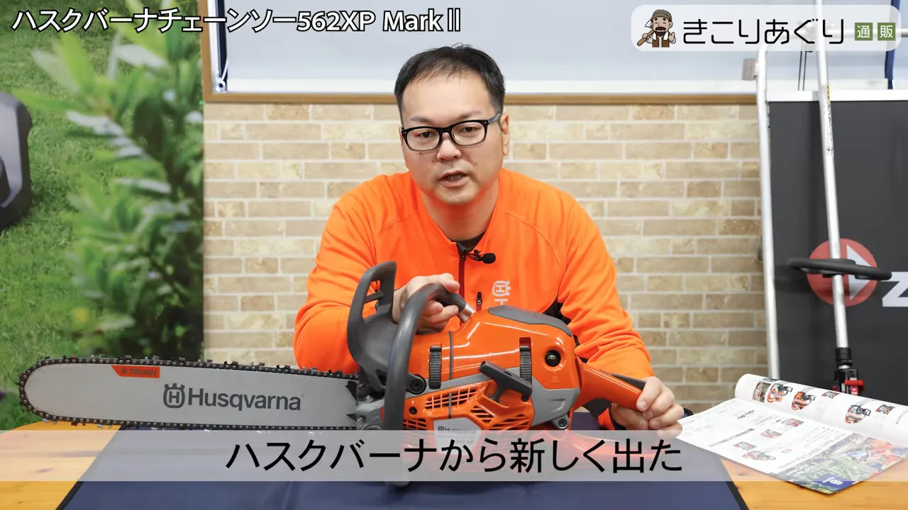 机の上に置かれたオレンジ色のハスクバーナ 562XP MarkⅡ とそれを手に持つプレゼンターの正面ショット。バーに Husqvarna ロゴが見える。
