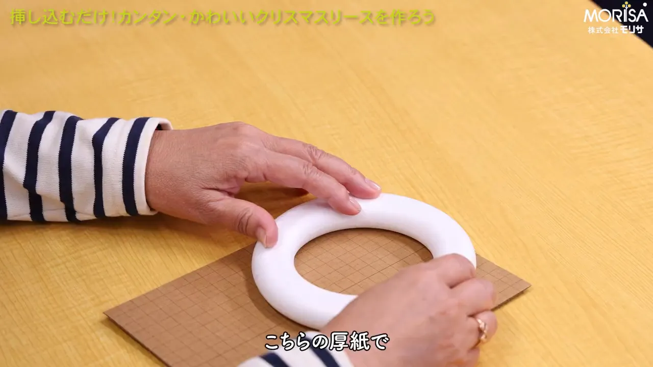 厚紙の上に発泡スチロールリース台をのせて位置を確認している手元(グリッドの厚紙が見える)