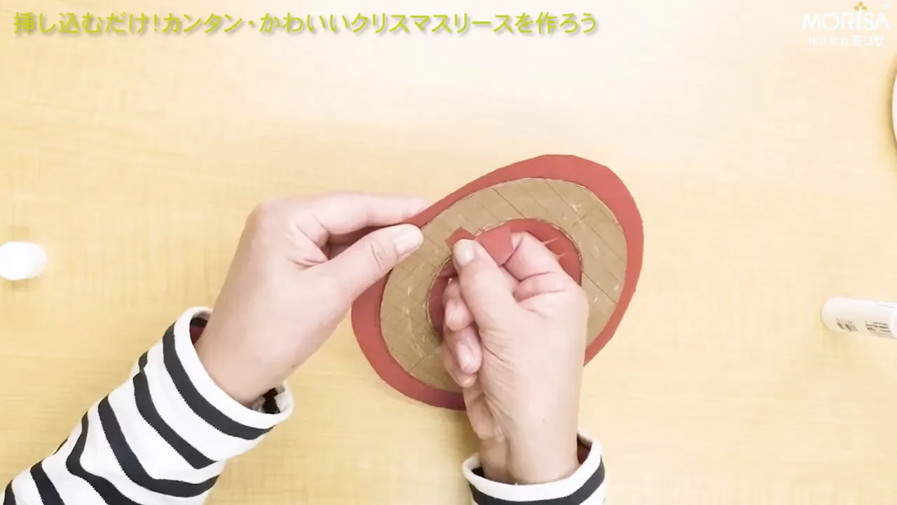 片手でリース土台を持ち、もう一方の手で和紙を折り返して整える作業のクローズアップ(斜め上から)