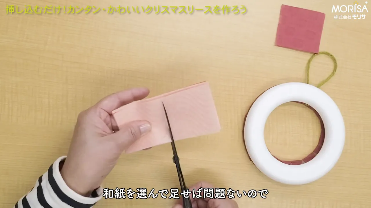 両手で和紙を持ち、ハサミでカットしている手元と右側に置かれた発泡スチロールのリース台の俯瞰写真