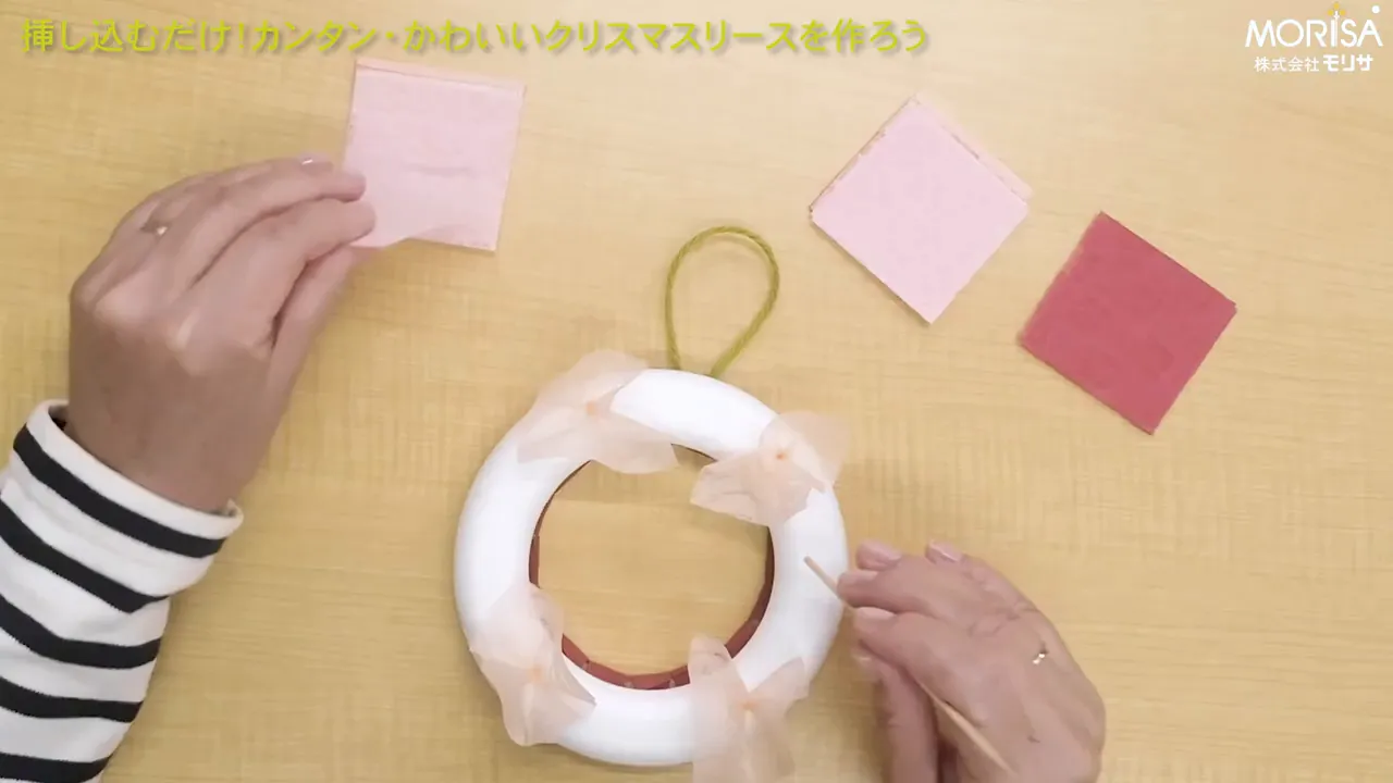 トップビューで撮影した作業風景。左手で和紙を持ち、右手で竹串を使って発泡スチロールリースに和紙を差し込もうとしている様子がはっきり見える。