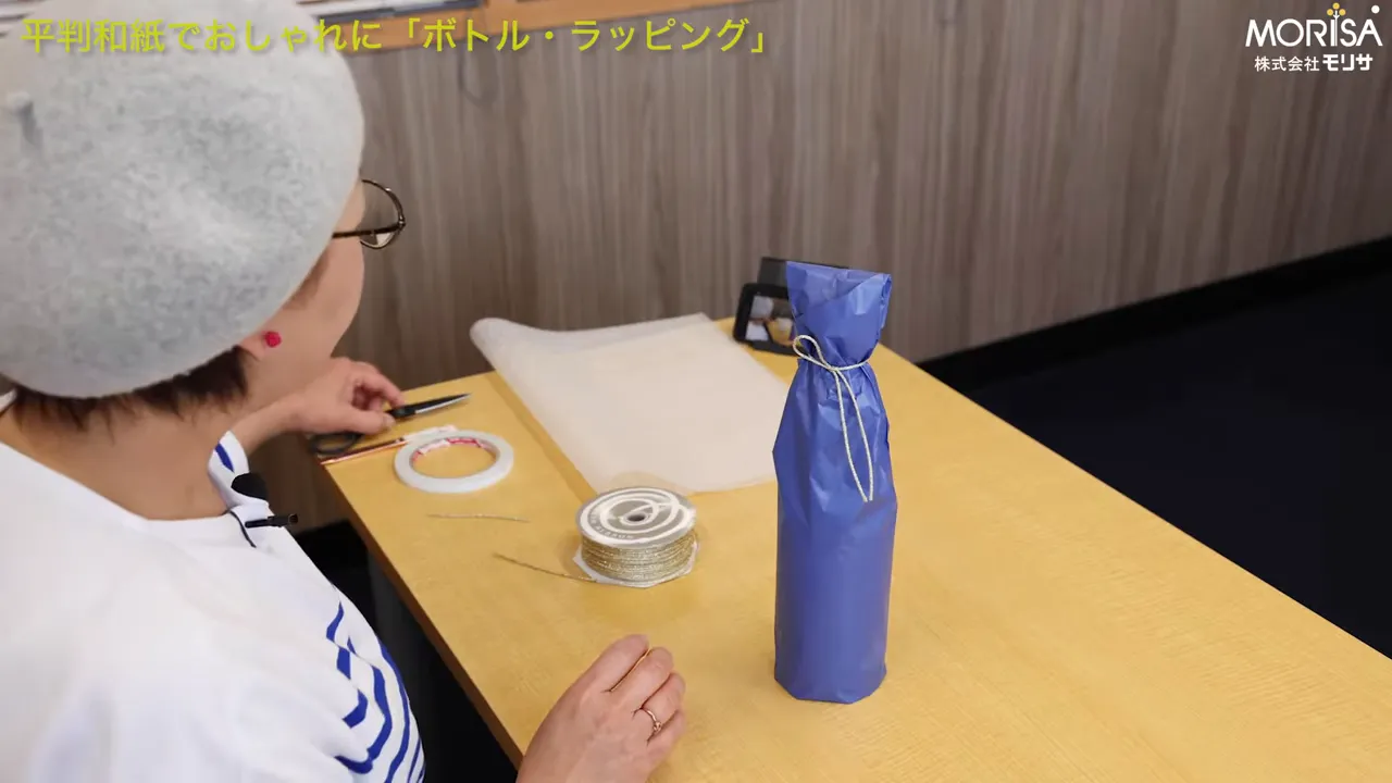 底折り後の青い包み紙で包んだボトルとテーブル上のはさみ・リボン・両面テープ