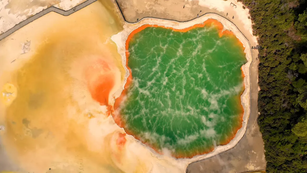 Aerial shot of a bright green geothermal pool with an orange rim and surrounding landscape