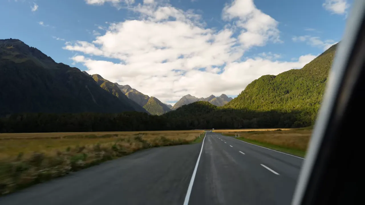 Open road on Milford Road with mountains and valley under blue sky