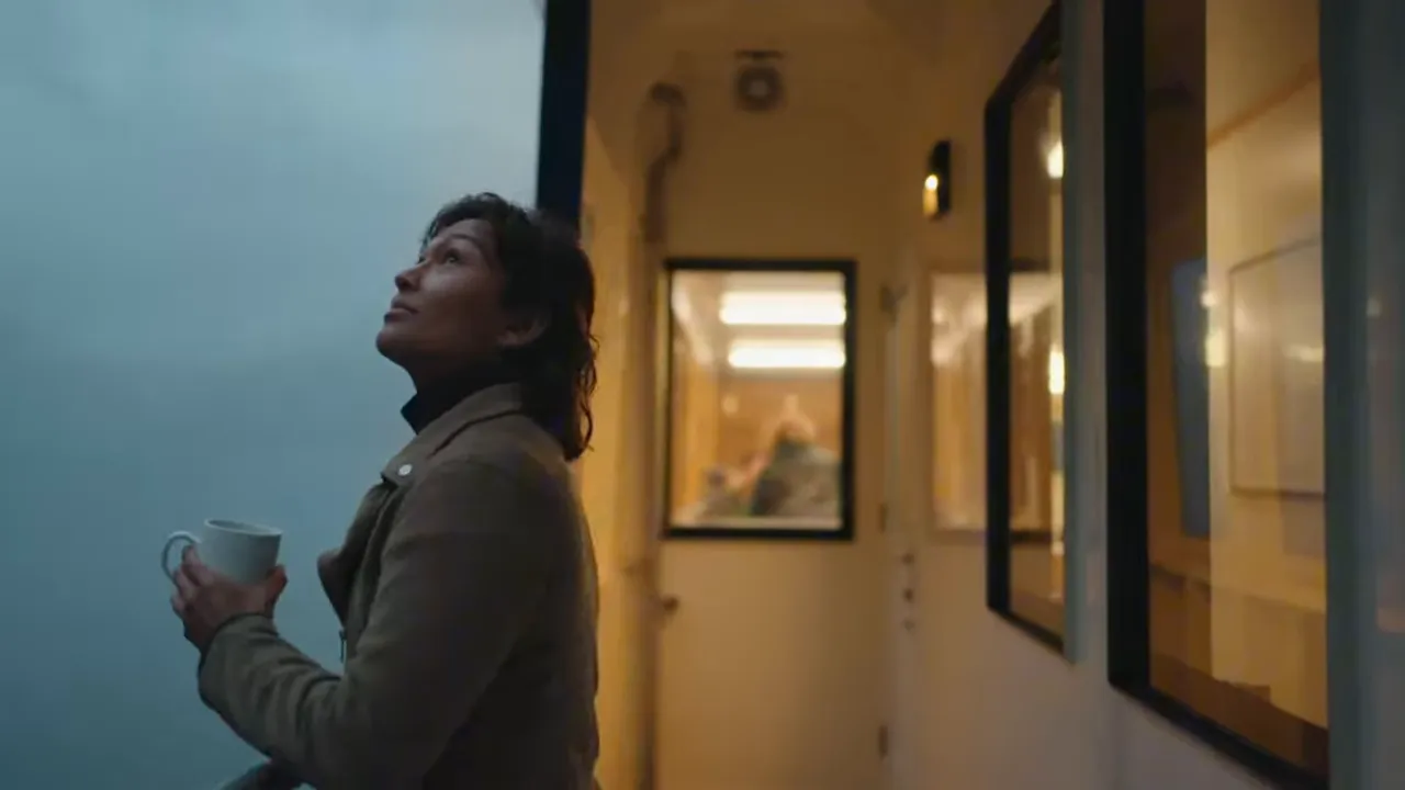 Guest on an overnight Milford Sound vessel standing on deck holding a mug, looking out at the fjord and misty water.