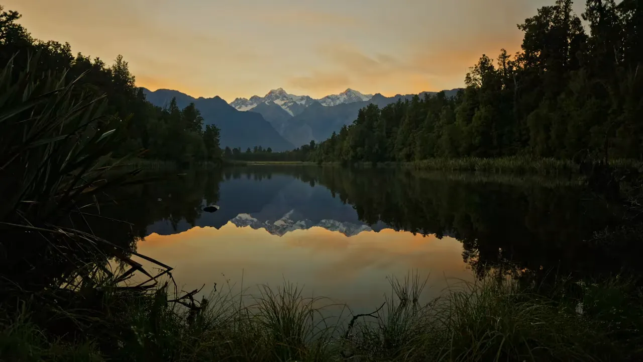 Snow-covered mountain peaks reflected in a still lake bordered by forest