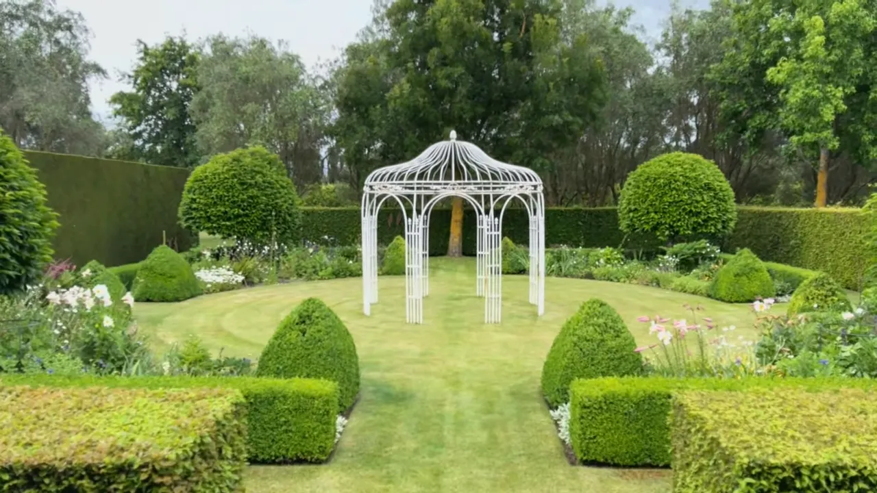 Wide view of a formal cottage garden showing clipped hedges, topiary and a white ornamental gazebo