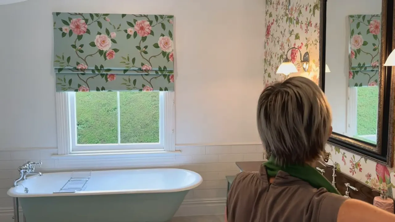 Freestanding clawfoot bathtub, floral window blind and vanity with mirror in a cottage bathroom