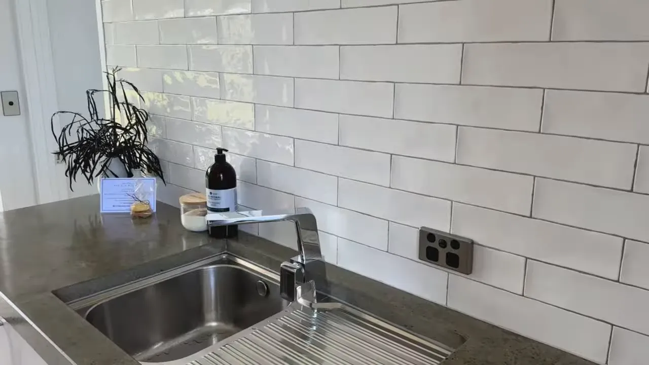 Kitchen sink, chrome faucet and tiled backsplash with countertop items at Glenburn Coastal Retreat