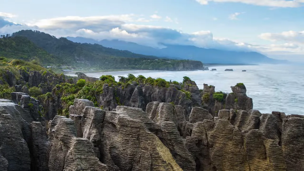 Layered pancake-like limestone rock formations at Punakaiki with the Tasman Sea and coastal hills in the background