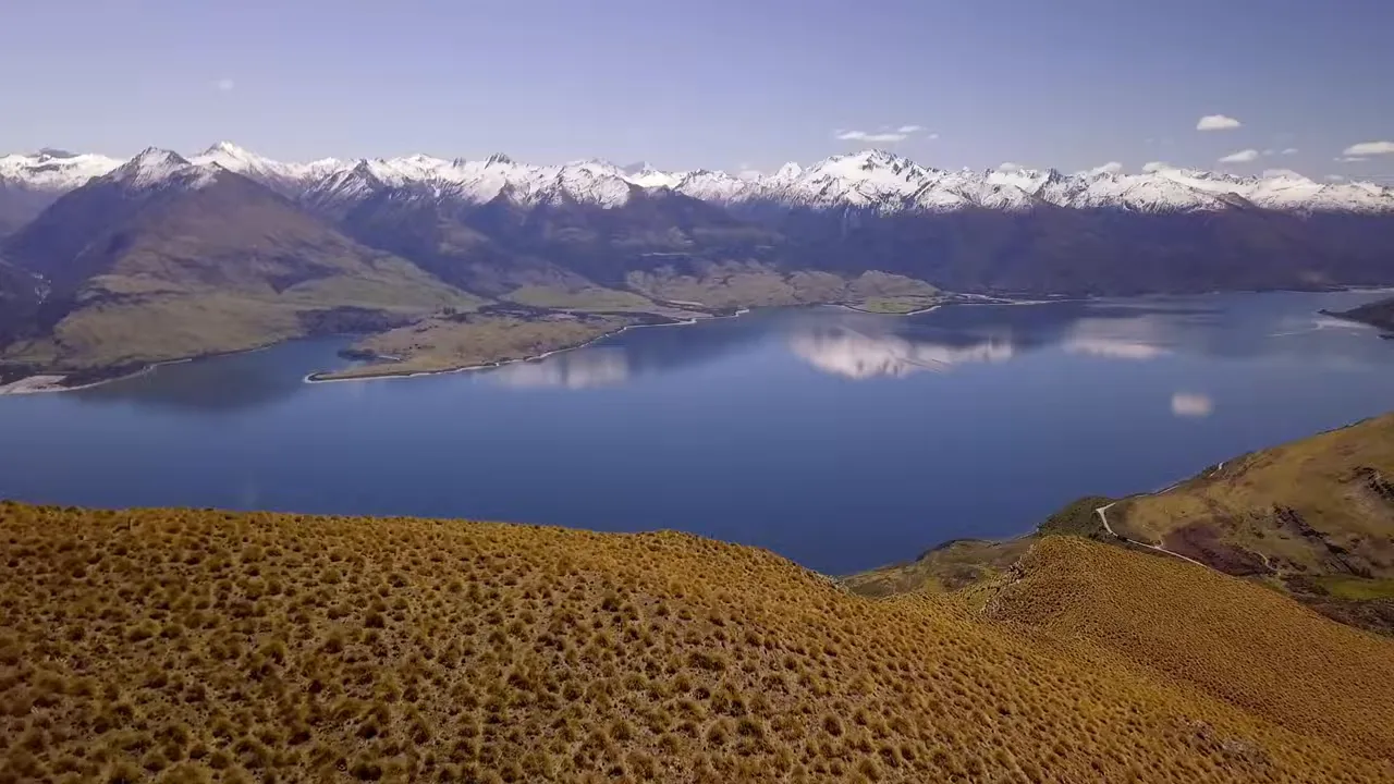 Panoramic view of an alpine lake with snow-capped mountains and tussock foreground