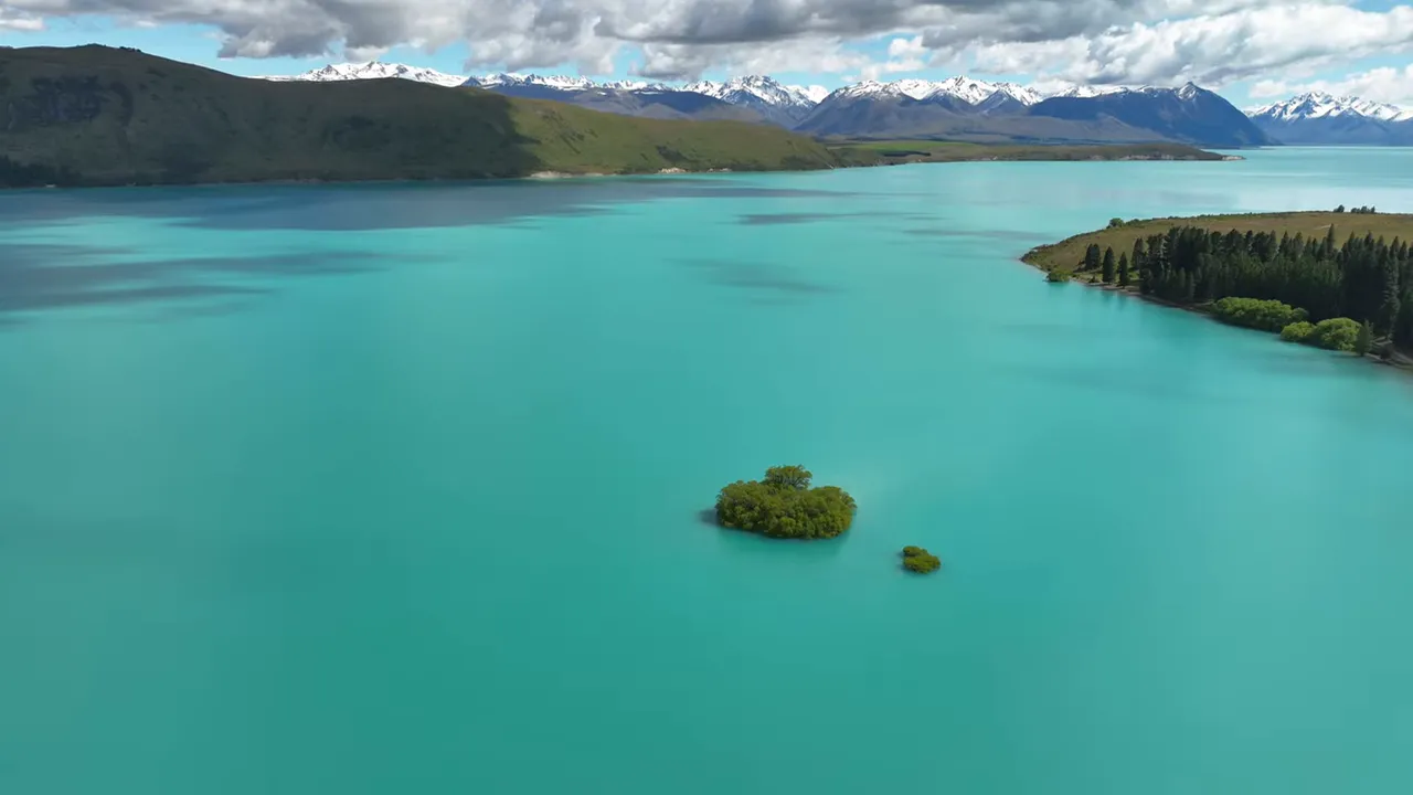 Aerial view of bright turquoise Lake Tekapo with a small island and distant snow-capped mountains