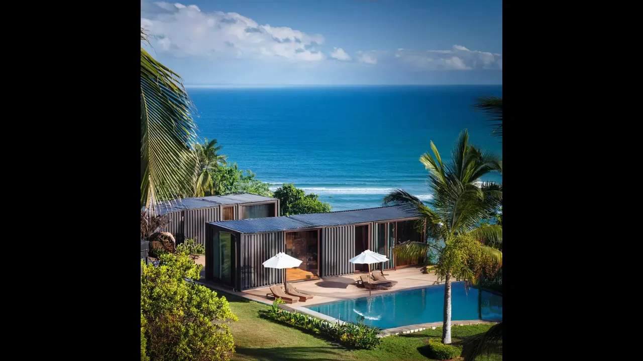 Low modern villa with lawn, pool umbrellas, and wide ocean backdrop