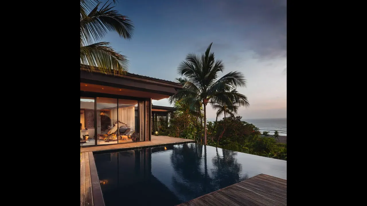 Modern pavilion-style villa with glass wall, wide deck, and tall palm trees