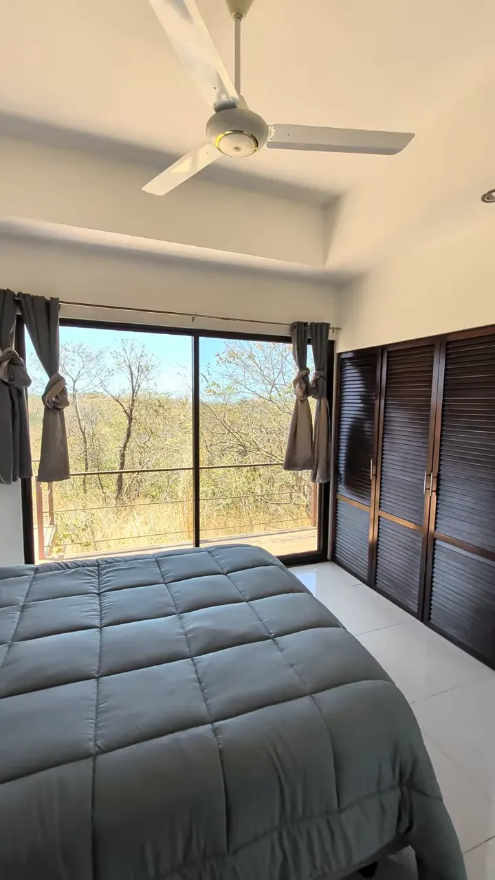 Primary bedroom with gray bedding, ceiling fan, sliding glass doors, and louvered closet doors