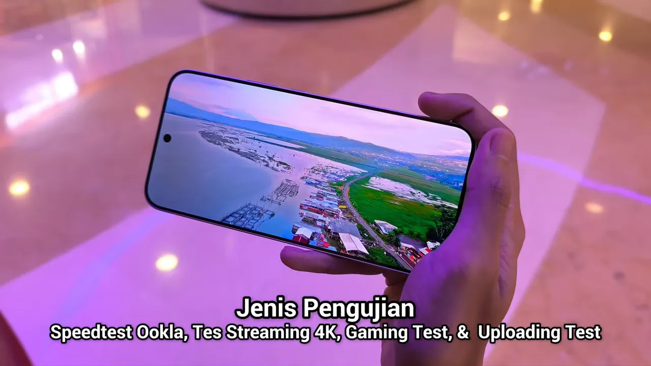 Tangan memegang smartphone yang menampilkan teks 'Jenis Pengujian: Speedtest Ookla, Tes Streaming 4K, Gaming Test, & Uploading Test' di layar