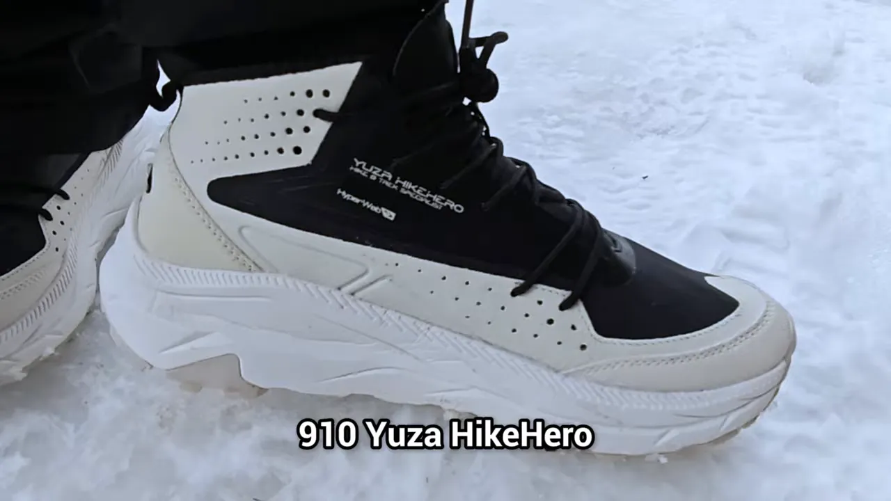 Close-up sepatu 910 Yuza HikeHero MID berwarna hitam-putih di atas salju dengan teks produk