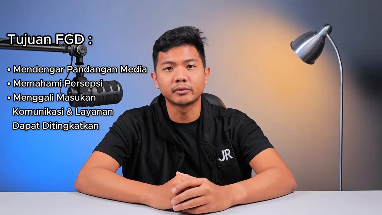 Pembicara di depan meja dengan daftar tujuan FGD yang terlihat di latar kiri: mendengar pandangan media, memahami persepsi, menggali masukan.