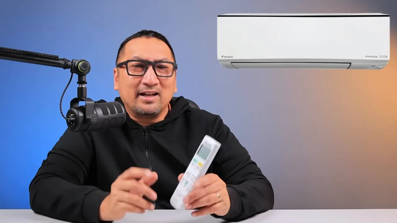 Daikin ALPHA Inverter unit indoor tampak depan dengan aksen garis hitam dan remote di tangan presenter