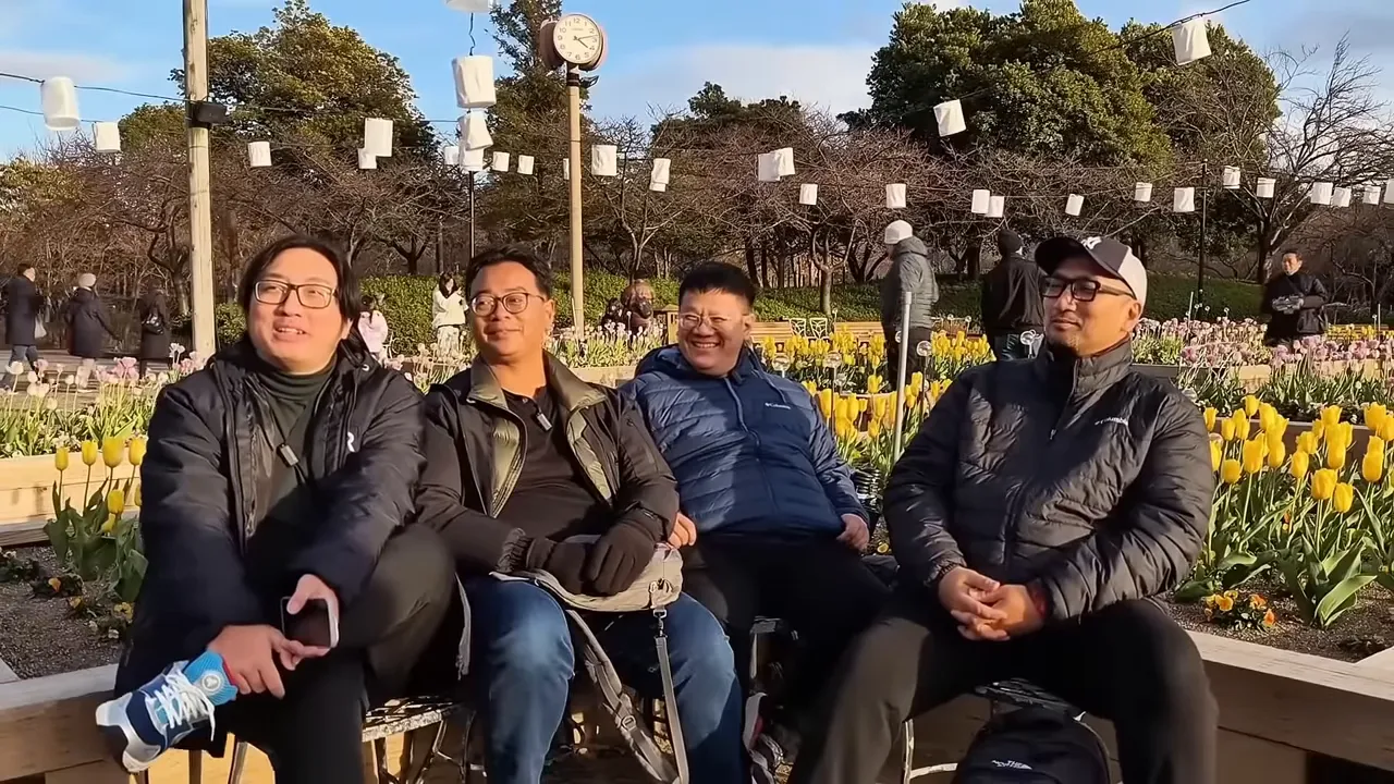 Empat pembicara duduk di bangku taman di depan deretan tulip, pencahayaan hangat dan komposisi seimbang.