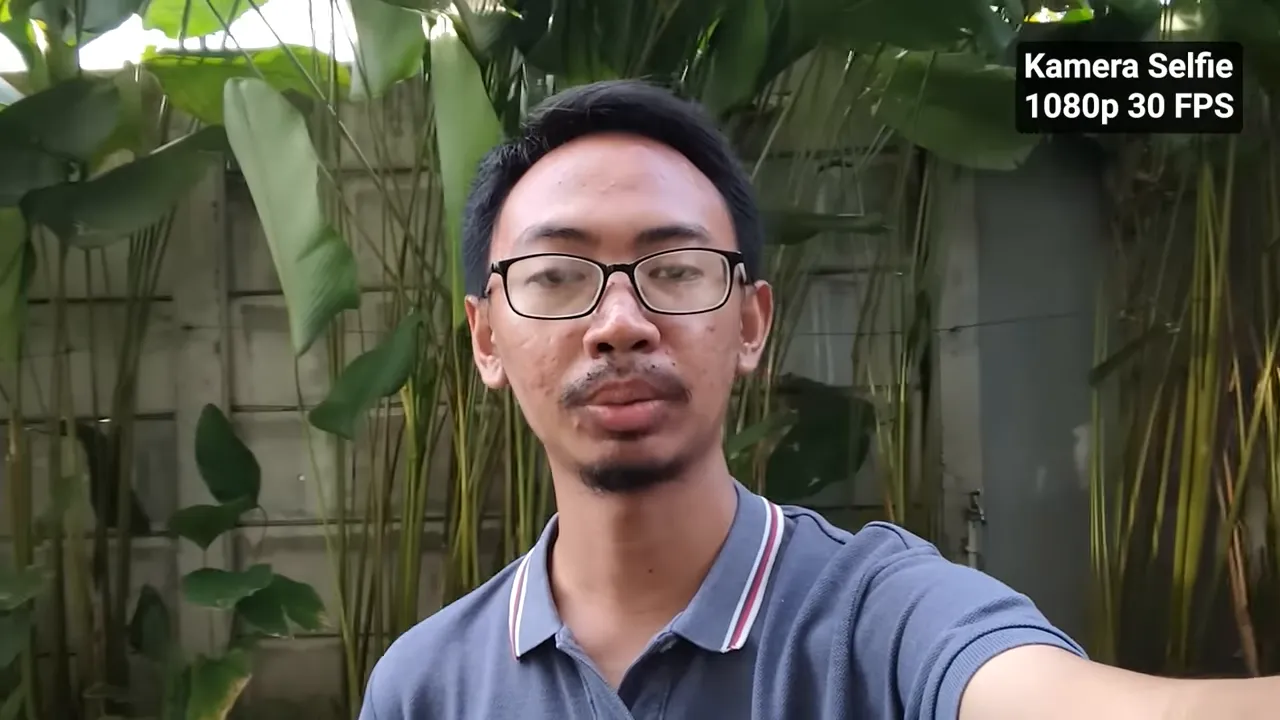 Close-up selfie siang hari menggunakan kamera depan Redmi Note 15 1080p 30fps, subjek fokus dengan latar tanaman hijau, teks overlay 'Kamera Selfie 1080p 30 FPS'.