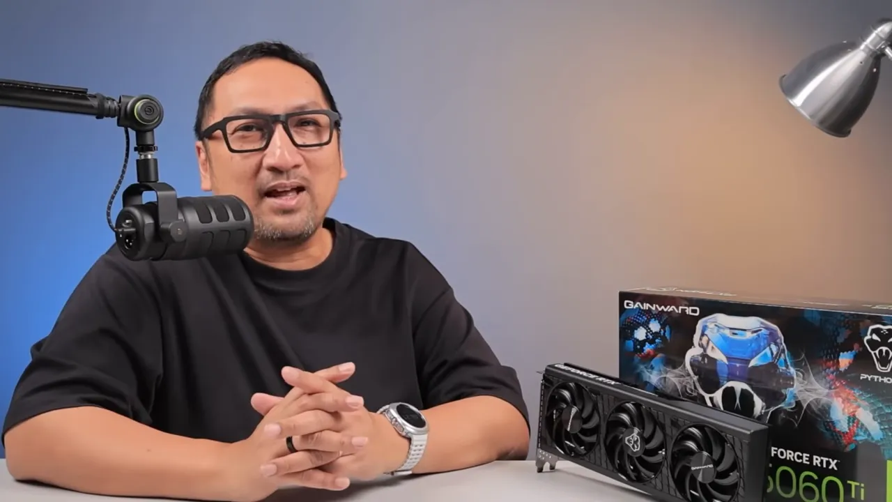 Reviewer duduk di meja bersama Gainward GeForce RTX 5060 Ti Python III 16 GB dan kotak produk terlihat jelas di sampingnya.