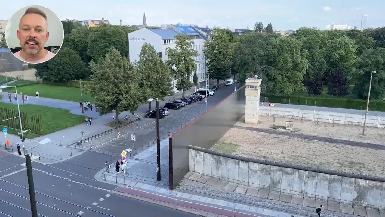 Bird's-eye view of the Berlin Wall Memorial showing the preserved concrete wall, a watchtower, adjacent green park and streets