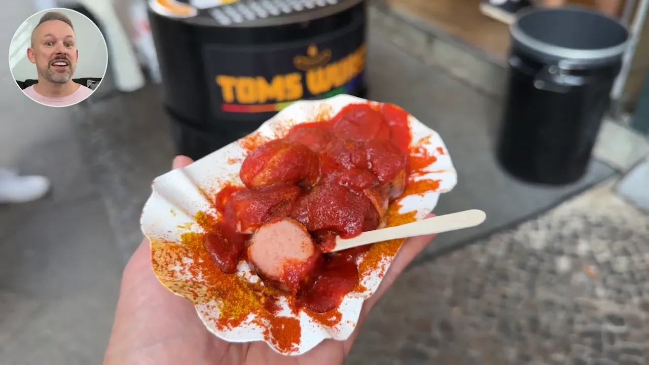 Hand holding a paper tray of currywurst topped with ketchup and curry powder