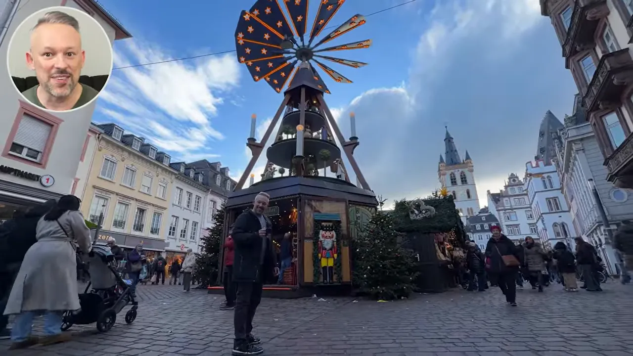 Wide-angle view of a Christmas market square in Trier featuring a tall wooden pyramid centerpiece, medieval buildings and shoppers.
