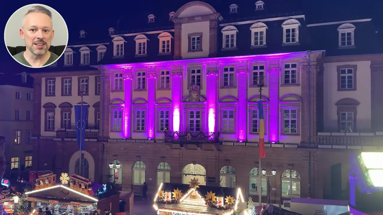 Historic town building illuminated in pink at night with Christmas market stalls and lights in the foreground