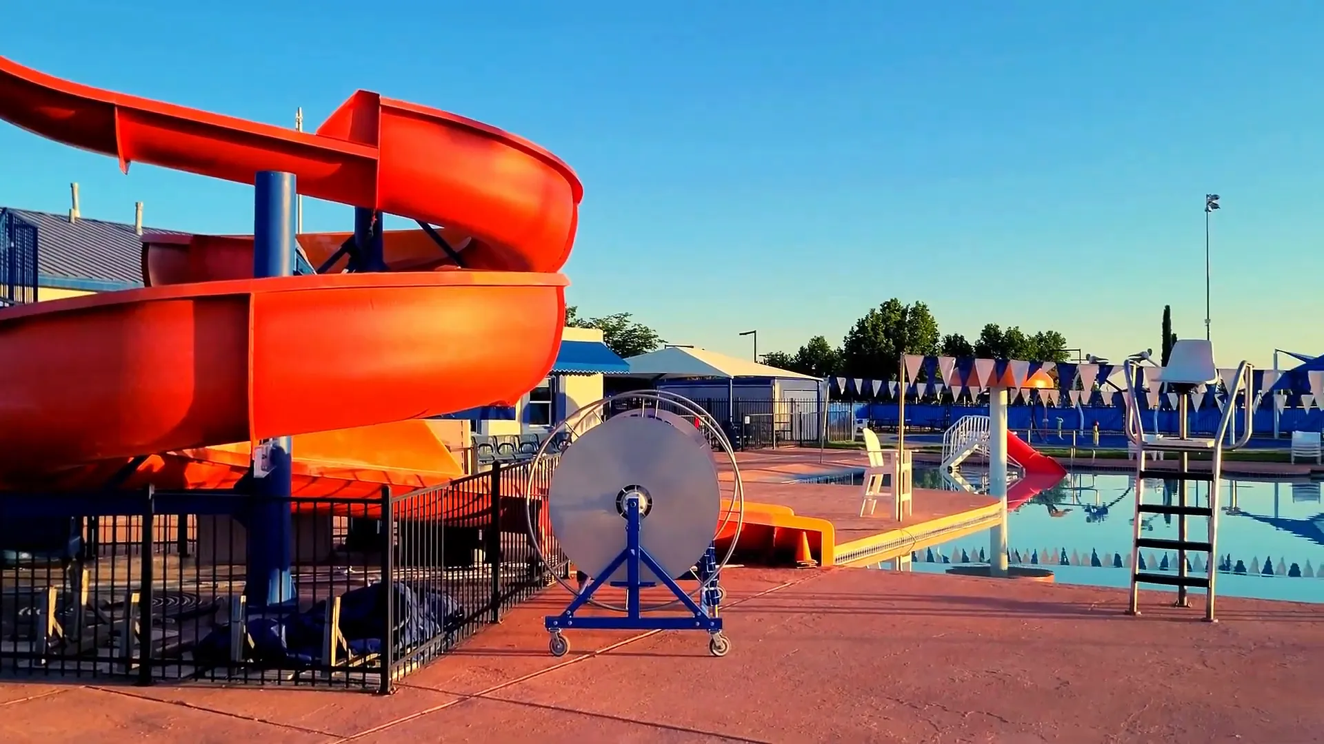 Neighborhood outdoor swimming pool showing a red water slide, pool deck, ladder and seating