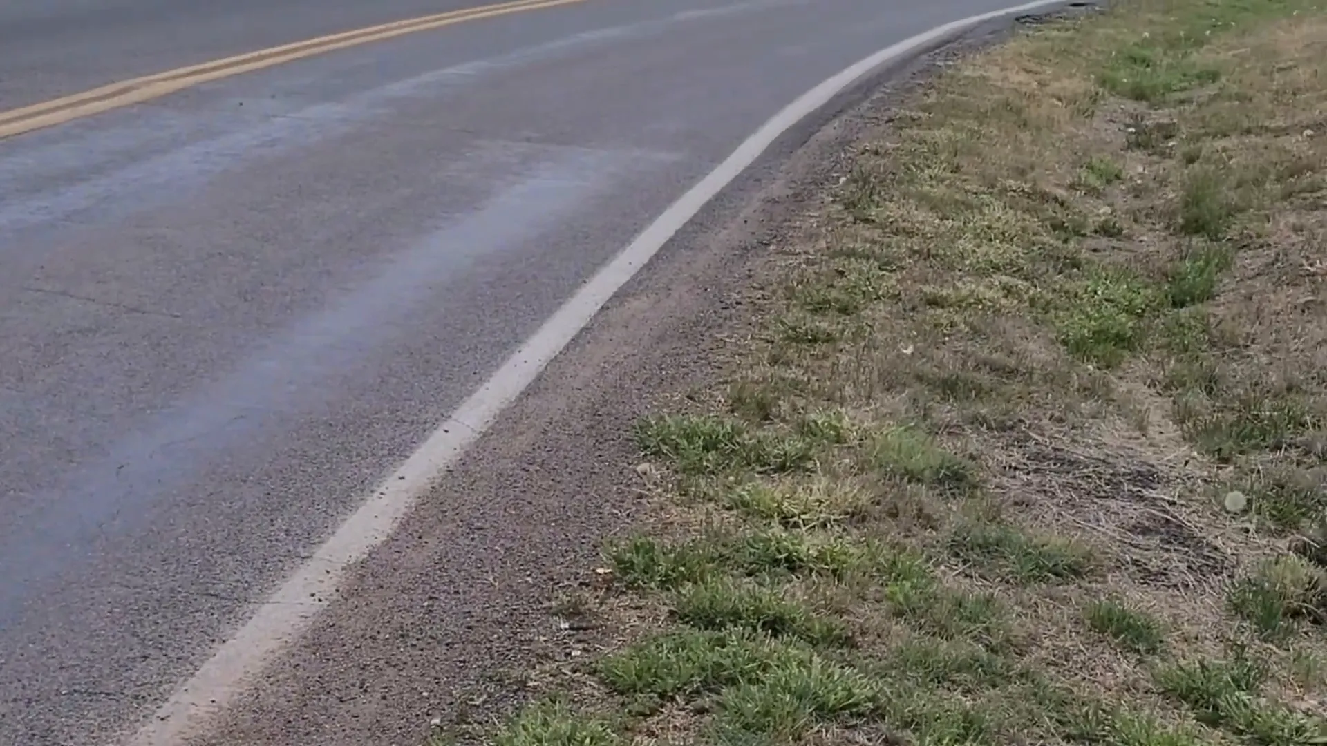Curved road with a grassy shoulder and curb where a sidewalk is missing