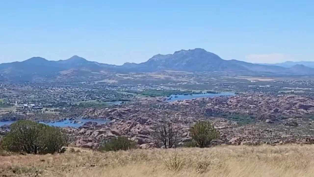 Panoramic hilltop view of rocky dells, lake and distant mountains near Prescott Valley