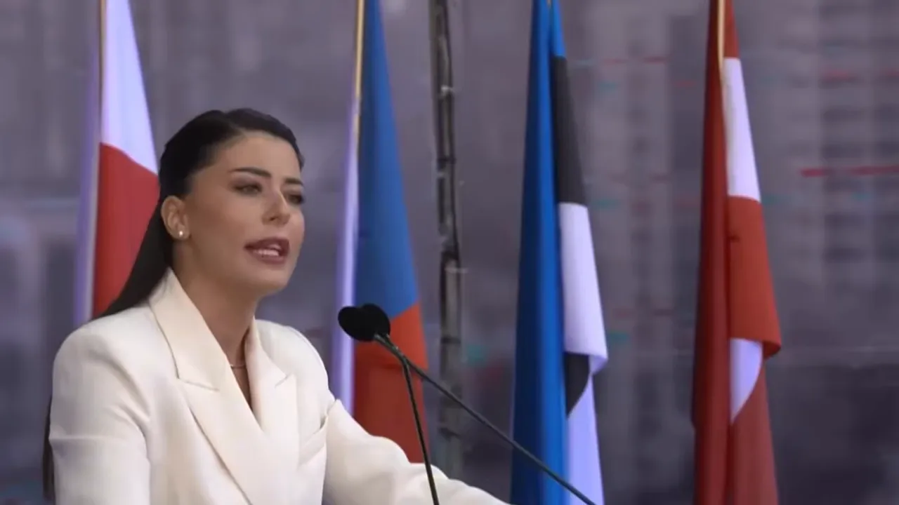 Afroditi Latinopoulou speaking at a podium with flags in the background