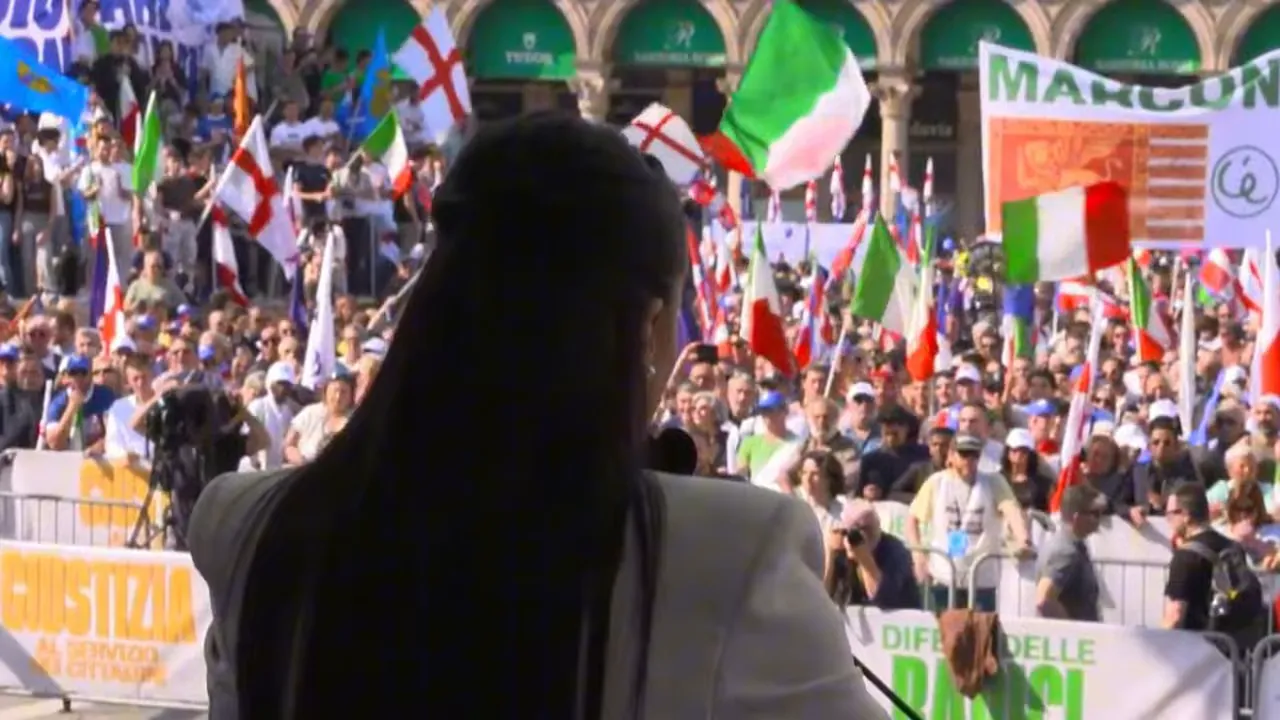 Crowd at a nationalist rally with flags seen from behind a speaker