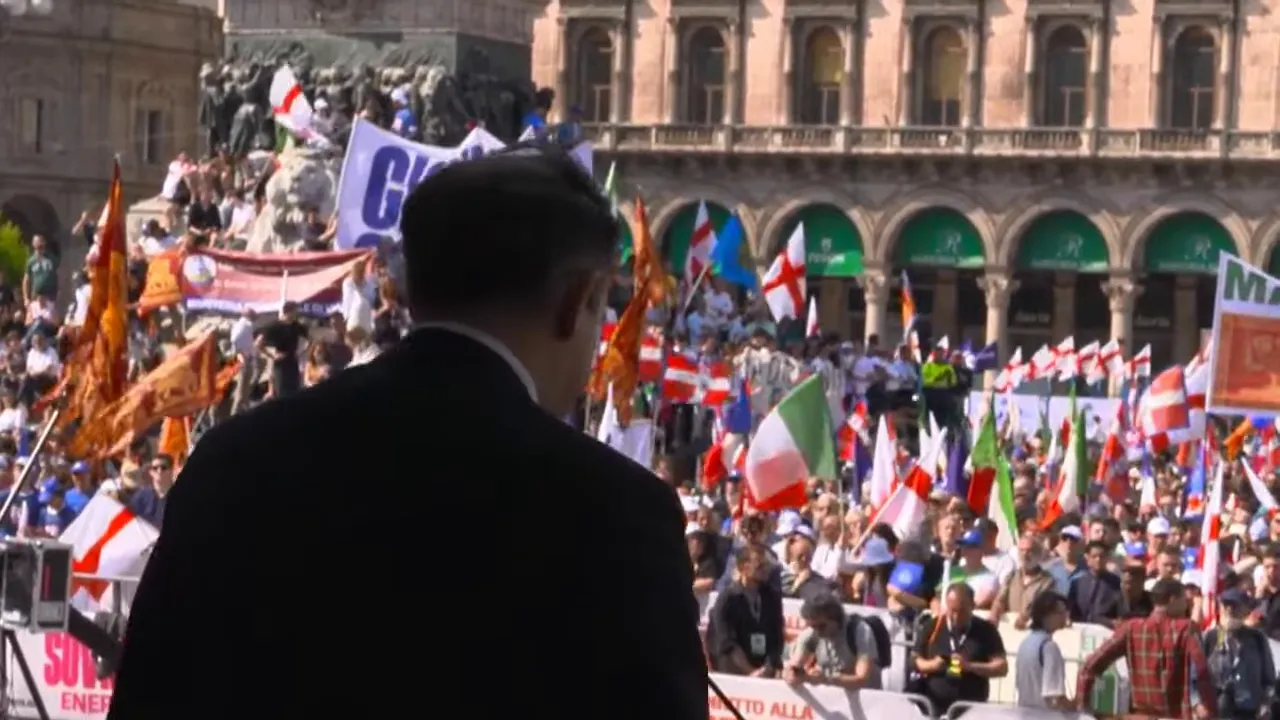 Crowd at a European political rally with flags behind a speaker in the foreground