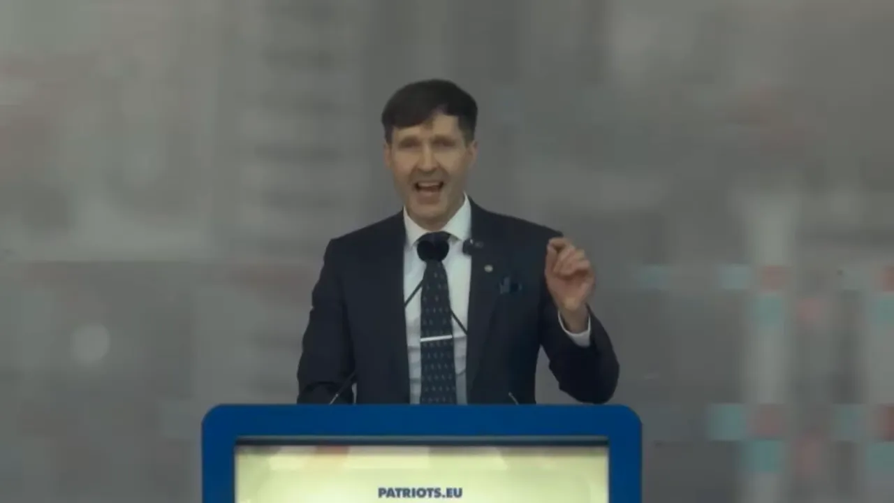 Man smiling and gesturing while speaking at a Patriots.eu podium with microphones