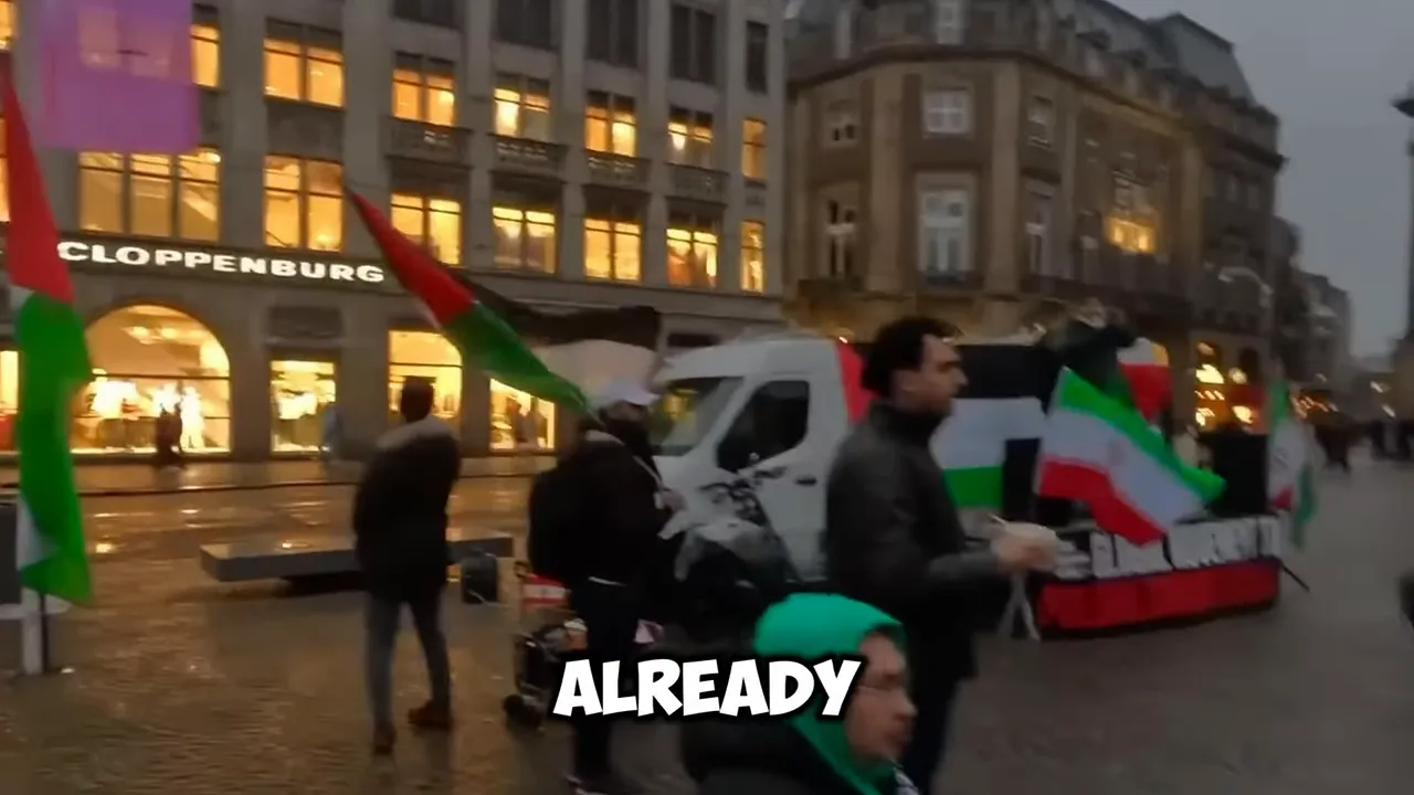 Protest march outside a building with flags held up and on-screen text