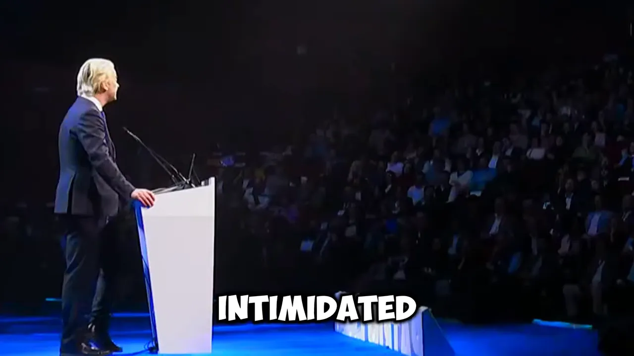 side view of speaker at podium facing a seated audience in a dark auditorium