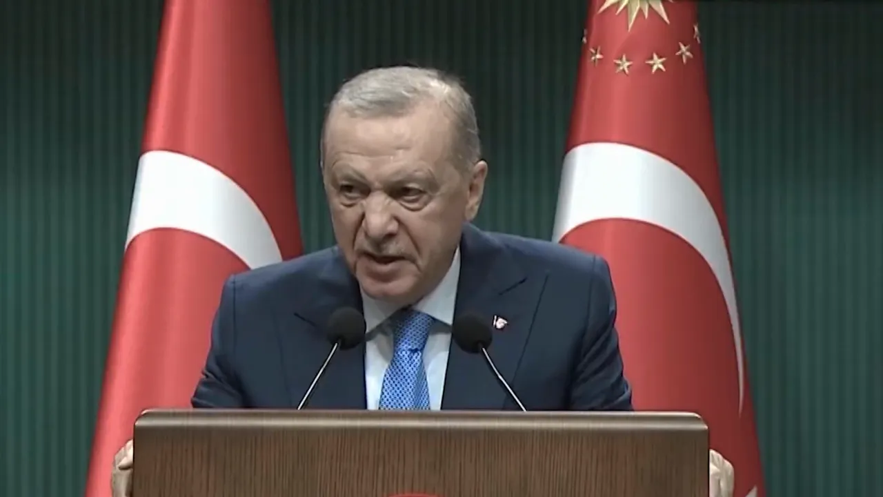 A senior official speaking at a podium with two national flags behind him.