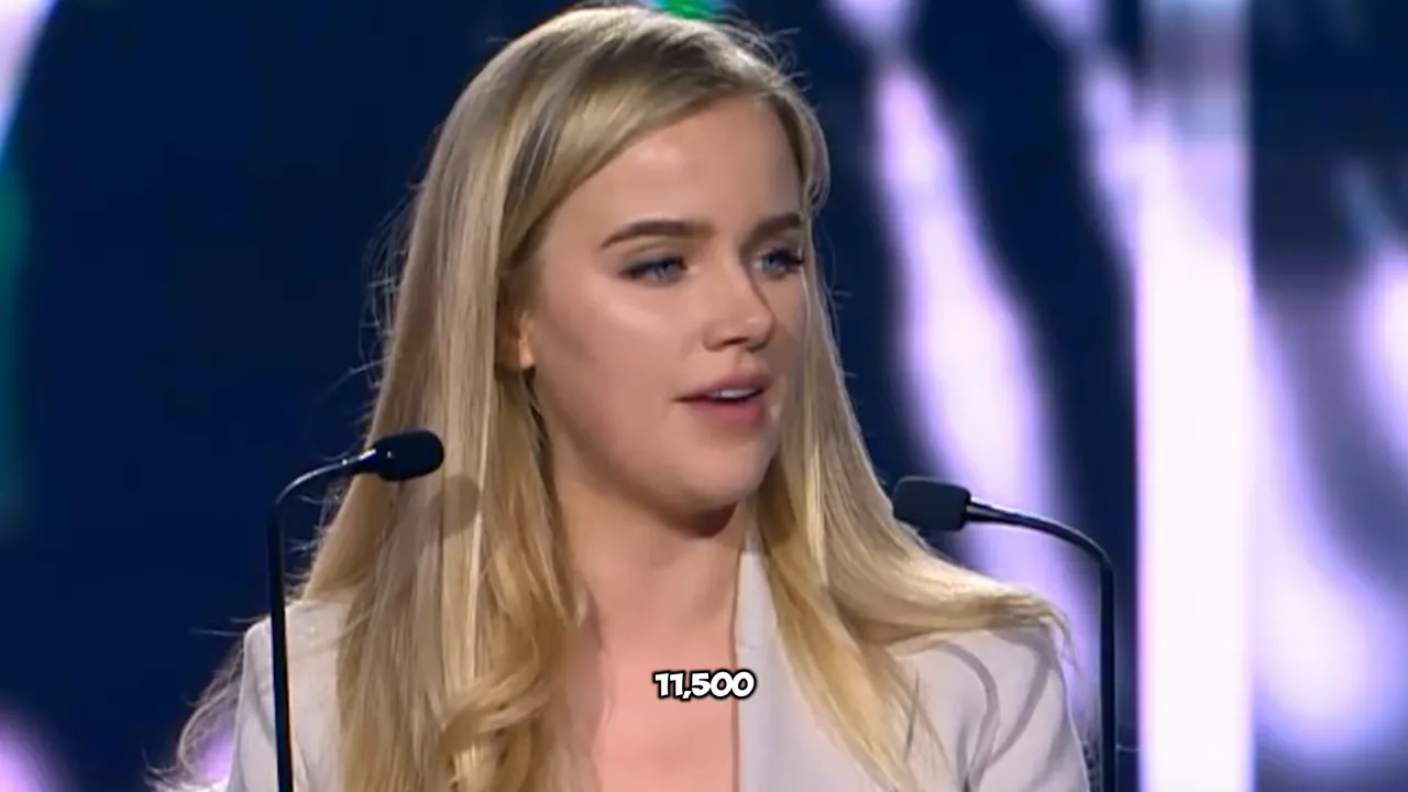 Eva Vlaardingerbroek speaking at a podium with stage lighting and microphones