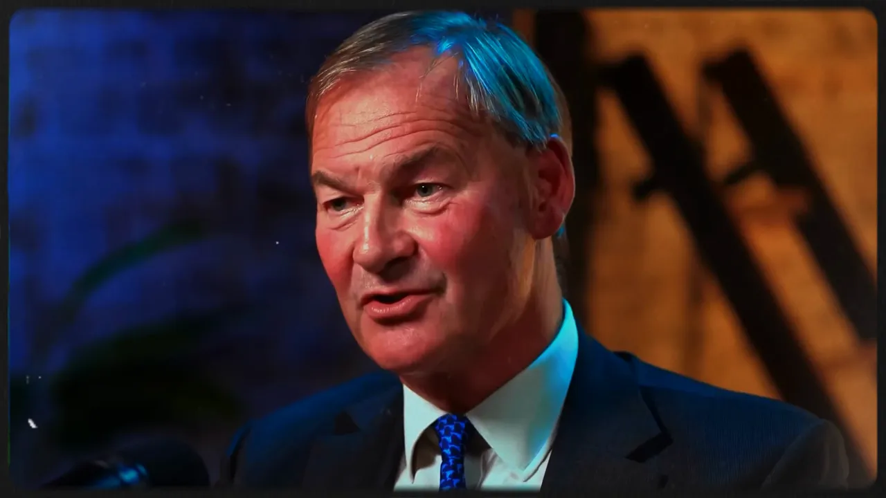 Man in suit speaking into a microphone, mid-shot, studio background