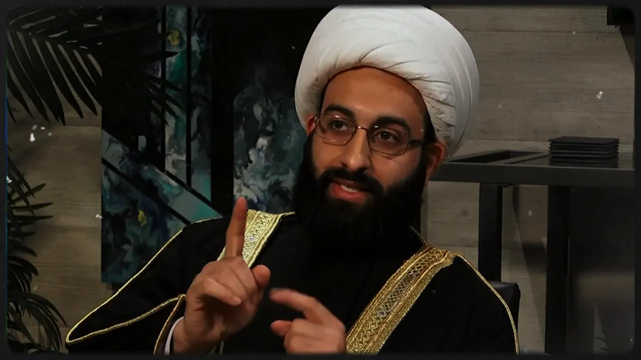 Religious scholar in traditional robes gesturing with a raised finger during an interview