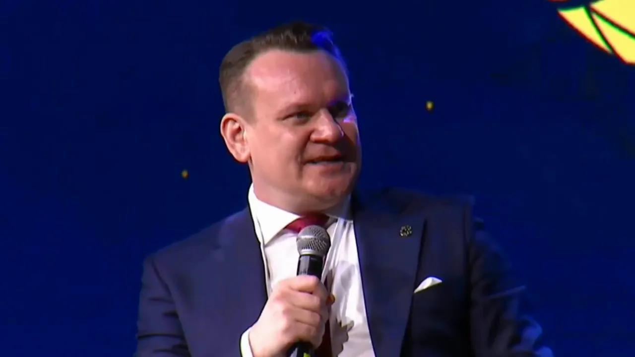 Politician speaking into a microphone on stage against a dark blue background